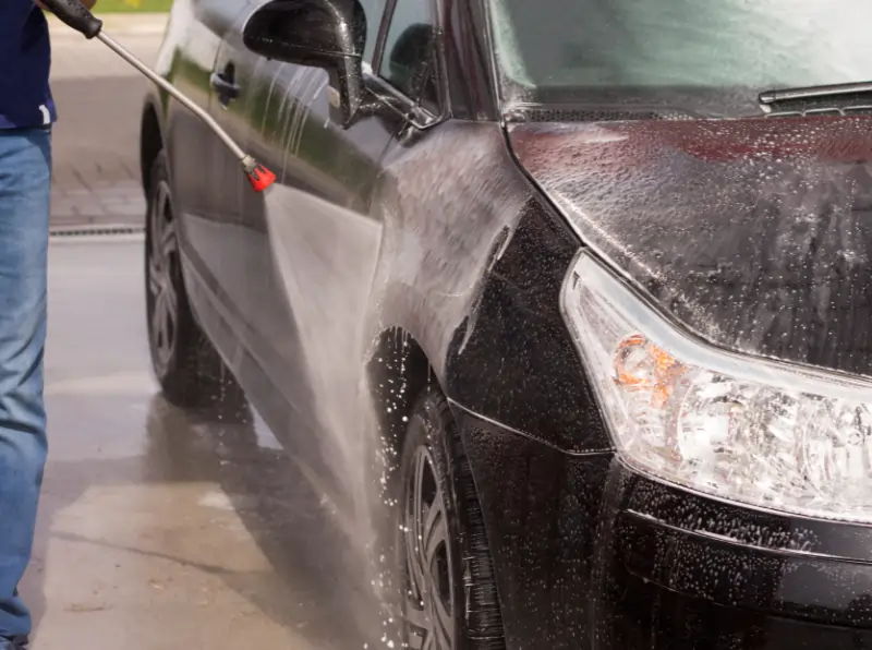 man spray rinsing car at car wash